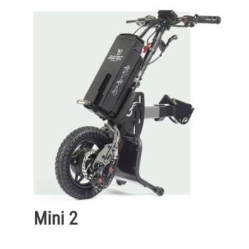 Handbike BATEC MINI 2 de color gris grafito plegado y anclado a una silla de ruedas manual, destacando su motor eléctrico.